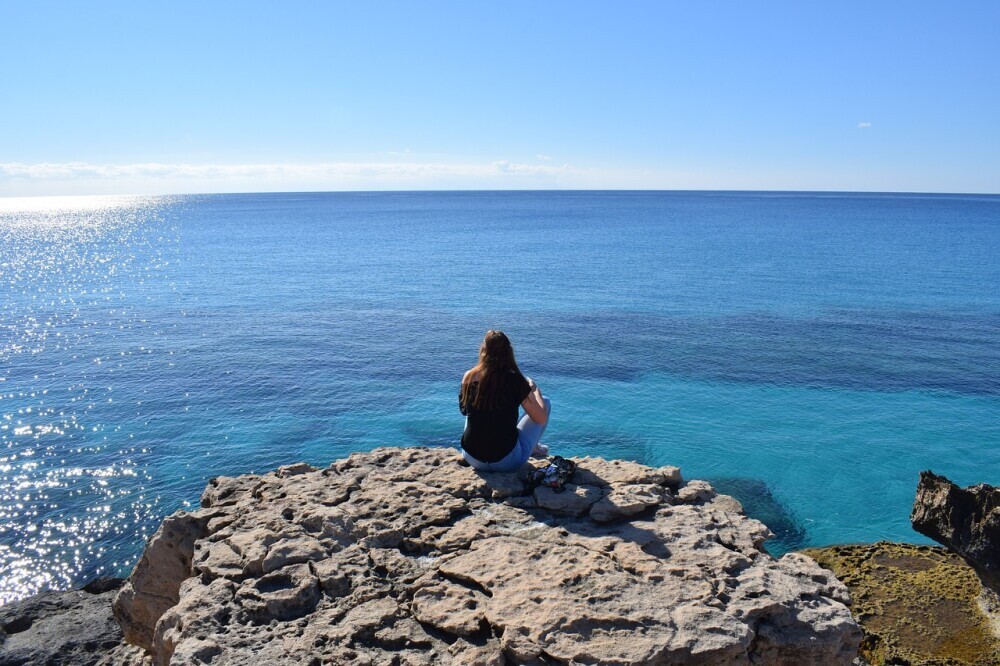 A solo female traveler sitting on a mountaintop, gazing at the horizon.